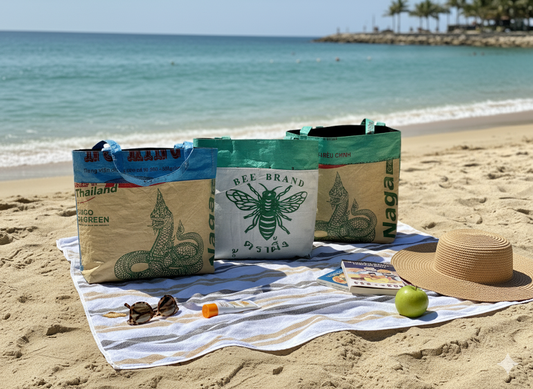 Three bags with bee designs on a beach towel on a sandy beach. Totes all from ShopTukTuk.com
