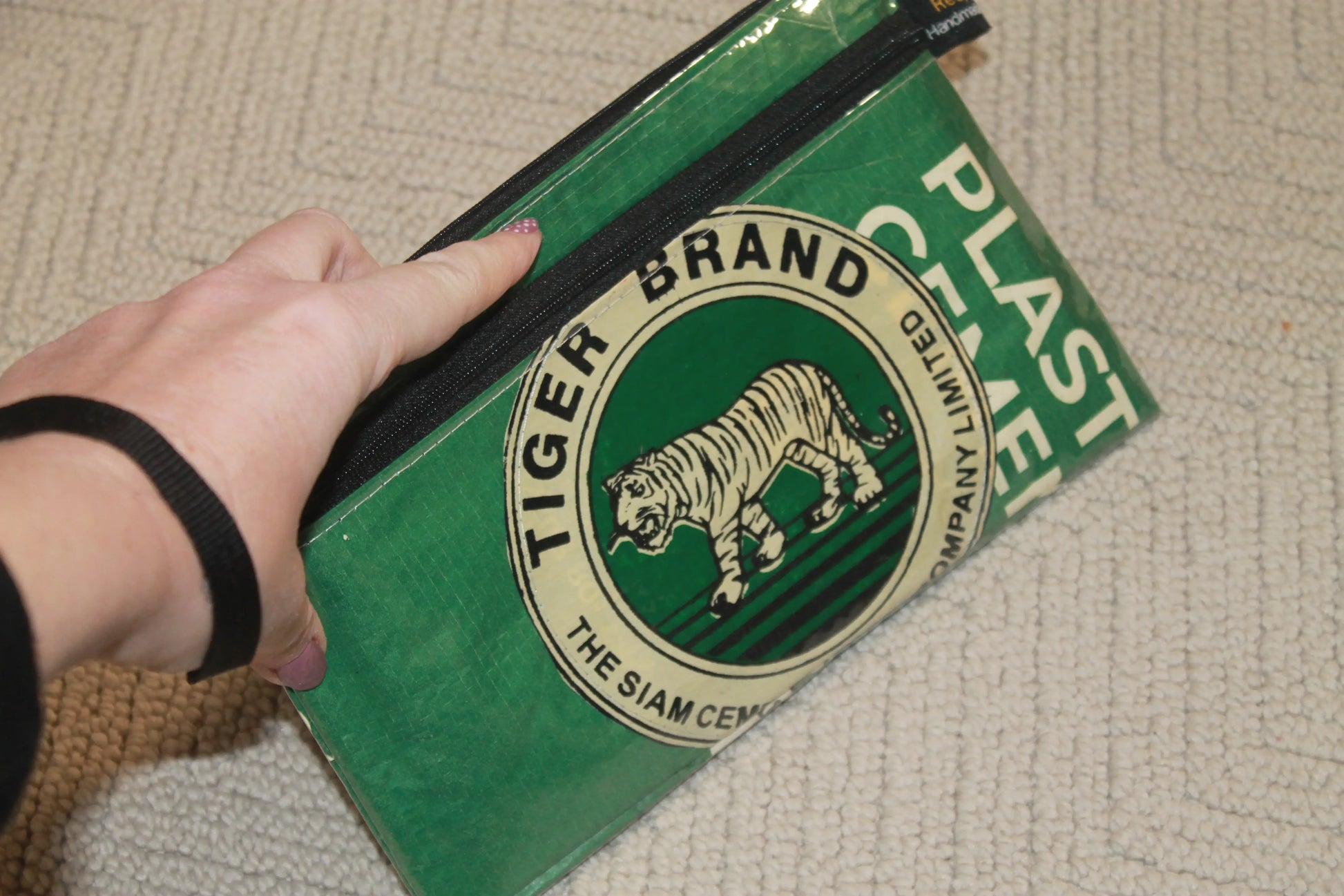 Green bag with Tiger Brand logo held by a hand on a textured surface from Tuk Tuk Trading